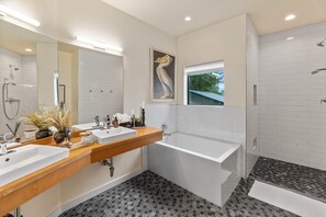 Un baño moderno con dos lavamanos, una bañera y una ducha.