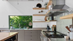 Une cuisine moderne dotée d’une grande fenêtre, d’appareils électroménagers intégrés et d’étagères en bois.