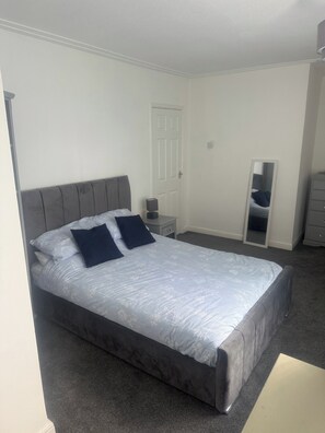 A bedroom with a bed, a nightstand, a dresser, a door, and a mirror. - Knotty Ash - 3 Beds - Sleeps 6 - On-site Parking (Liverpool)