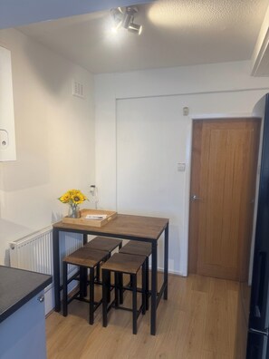 Une petite cuisine avec une table en bois, deux tabourets, un radiateur et une porte.