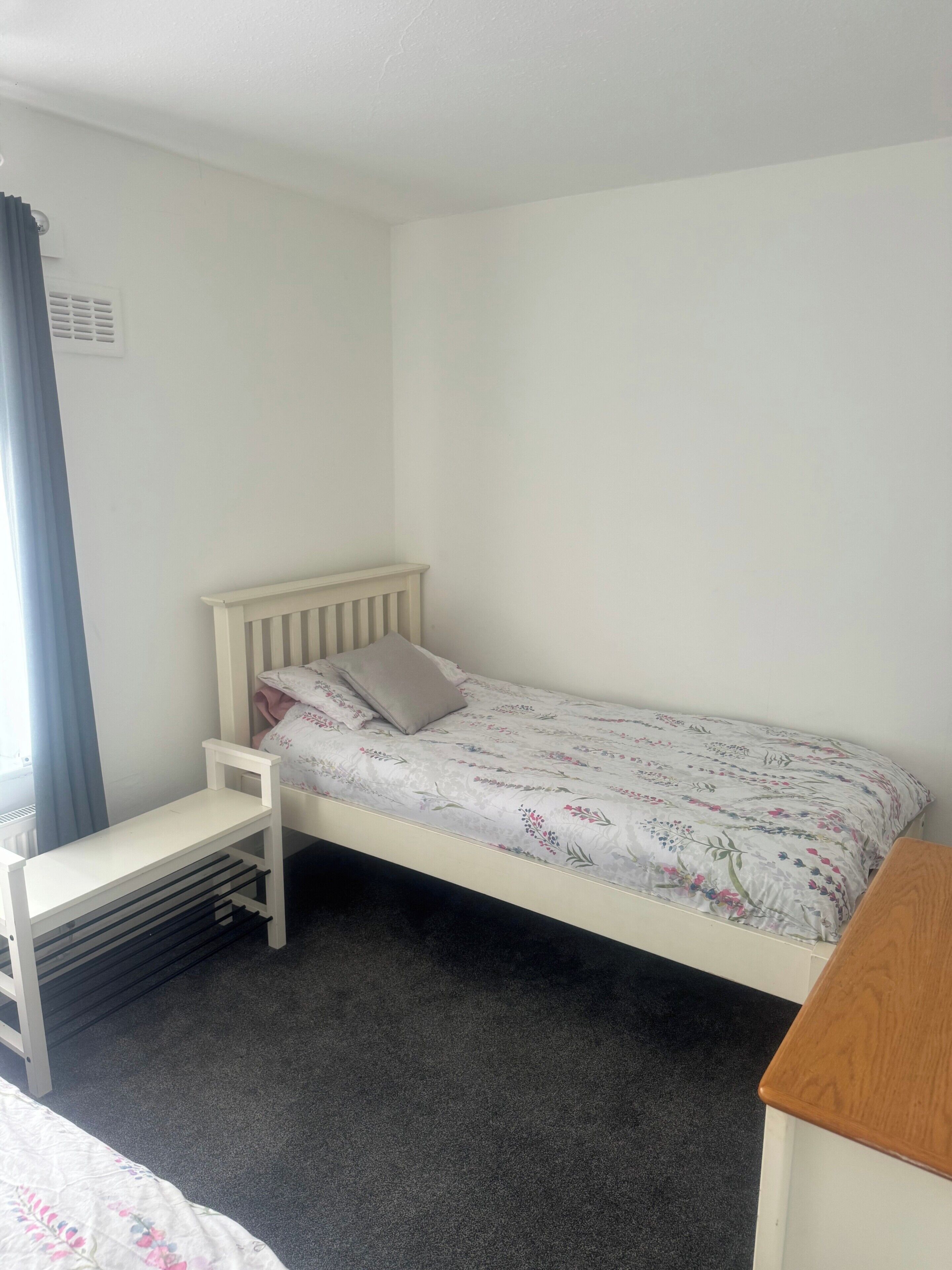 A single bed with a floral bedspread, a small white bedside table, and a chair.