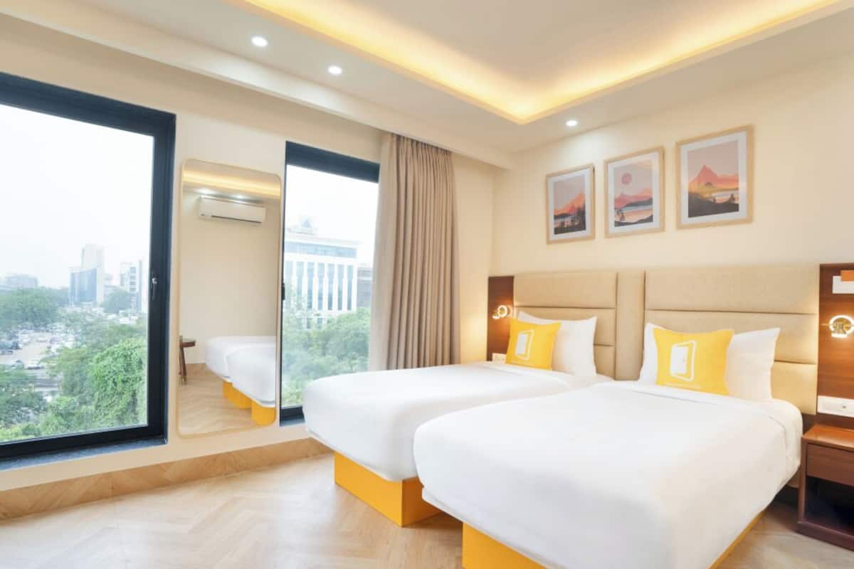 A hotel room with two beds, a large window with a city view, and artwork on the wall.