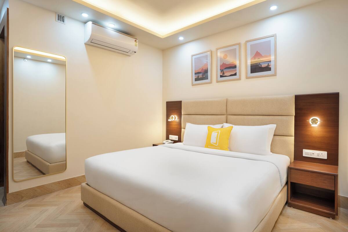 A modern hotel room with a large bed, bedside tables, a mirror, and wall-mounted artwork.
