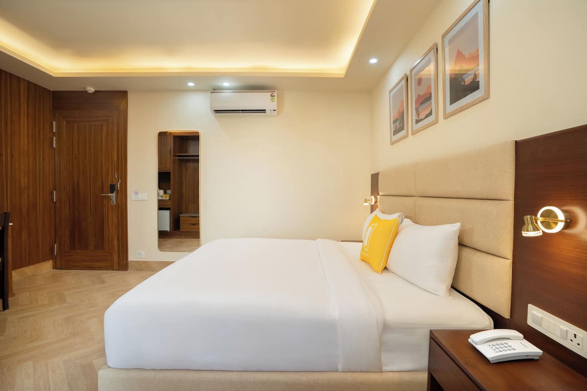 A hotel room with a large bed, a bedside table with a phone, an air conditioning unit, and a wooden wardrobe.