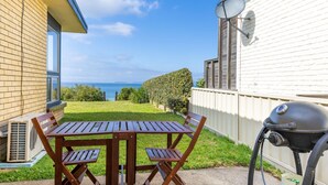 Un patio con mesa y sillas, una parrilla y vistas al mar.