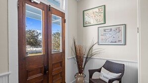 Eine Holztür mit Glasfeldern, ein Korbsessel mit Kissen mit dem Aufdruck 'home' und zwei gerahmte Karten an der Wand.