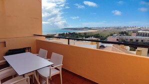A balcony with a table and chairs, overlooking a beach and cityscape.
