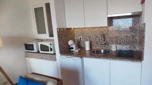 A compact kitchen with white cabinets, a granite countertop, a microwave, a coffee maker, and a sink.