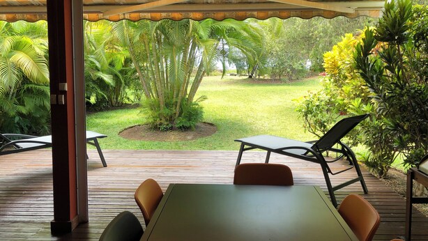 Une terrasse extérieure avec une table et des chaises, entourée d’une végétation luxuriante et offrant une vue sur un jardin bien entretenu.