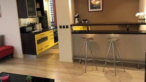 Une cuisine moderne avec des meubles de couleur jaune, un plan de travail noir et un coin bar équipé de deux tabourets.
