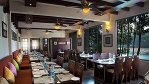 A restaurant with a long dining table set for a meal, surrounded by chairs. - The Wave Wayanad Resort (Sulthan Bathery)