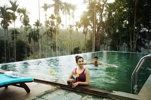 Una piscina con due persone, circondata da alte palme.