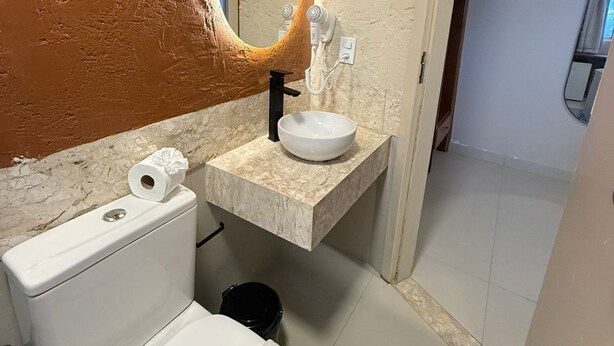 Een badkamer met een wit toilet, een marmeren wastafel, een spiegel met verlichting en een handdoek op de vloer.