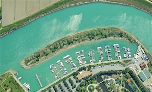 An aerial view of a marina with numerous boats docked, surrounded by greenery and a curved shoreline.