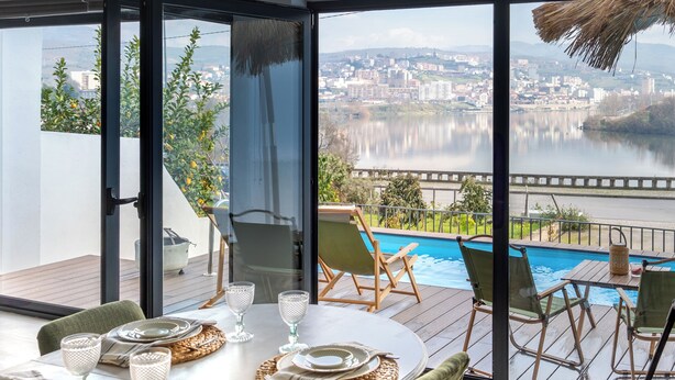 Un comedor con una mesa dispuesta para cuatro personas, con vistas a una piscina y al paisaje urbano.