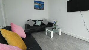 A modern living room with a black sofa, a glass coffee table, and a painting on the wall. - Sefton House by Smart Corporate Stays (Liverpool)