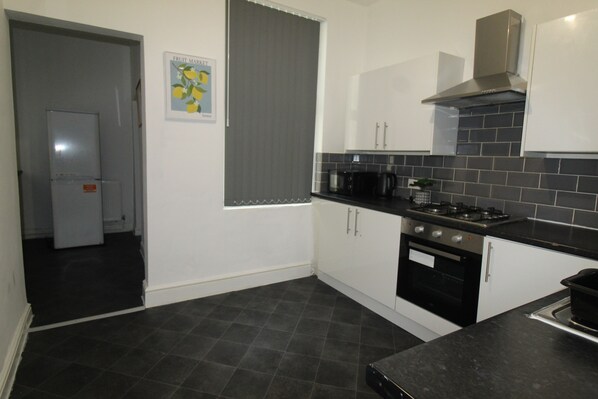 A kitchen with a black tiled backsplash, white cabinets, a stainless steel range hood, and a black countertop.