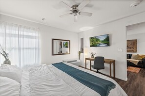 A hotel room with a bed, a desk, a chair, a TV, and a painting on the wall. - Overland Park Apartment King Bed, Workspace, & Gym (Overland Park)