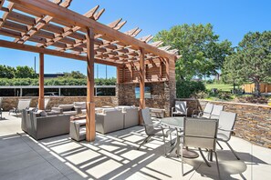 An outdoor patio with a pergola, wicker furniture, and a stone wall. - Overland Park Apartment King Bed, Workspace, & Gym (Overland Park)