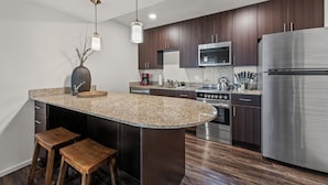 Una cocina moderna con armarios de madera oscura, un refrigerador de acero inoxidable, encimeras de granito y una isla central con taburetes.