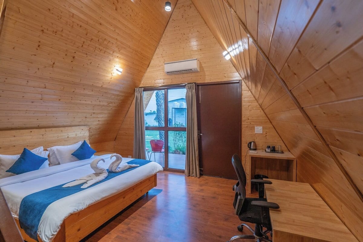 Quarto de madeira com uma cama, uma escrivaninha e vista através de uma porta de vidro.
