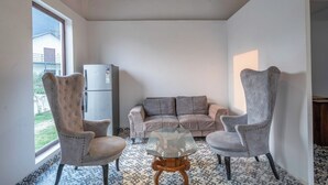 Ein Zimmer mit einer Couch, zwei Sesseln, einem Glastisch, einem Kühlschrank und einem Bodenbelag mit Muster.