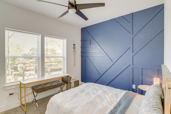 A bedroom with a bed, a desk, and a chair. There is a window with blinds, a ceiling fan, and a wall with geometric patterns. - Sleek Home w/ Screened Patio & Yard in Houston! (Houston)