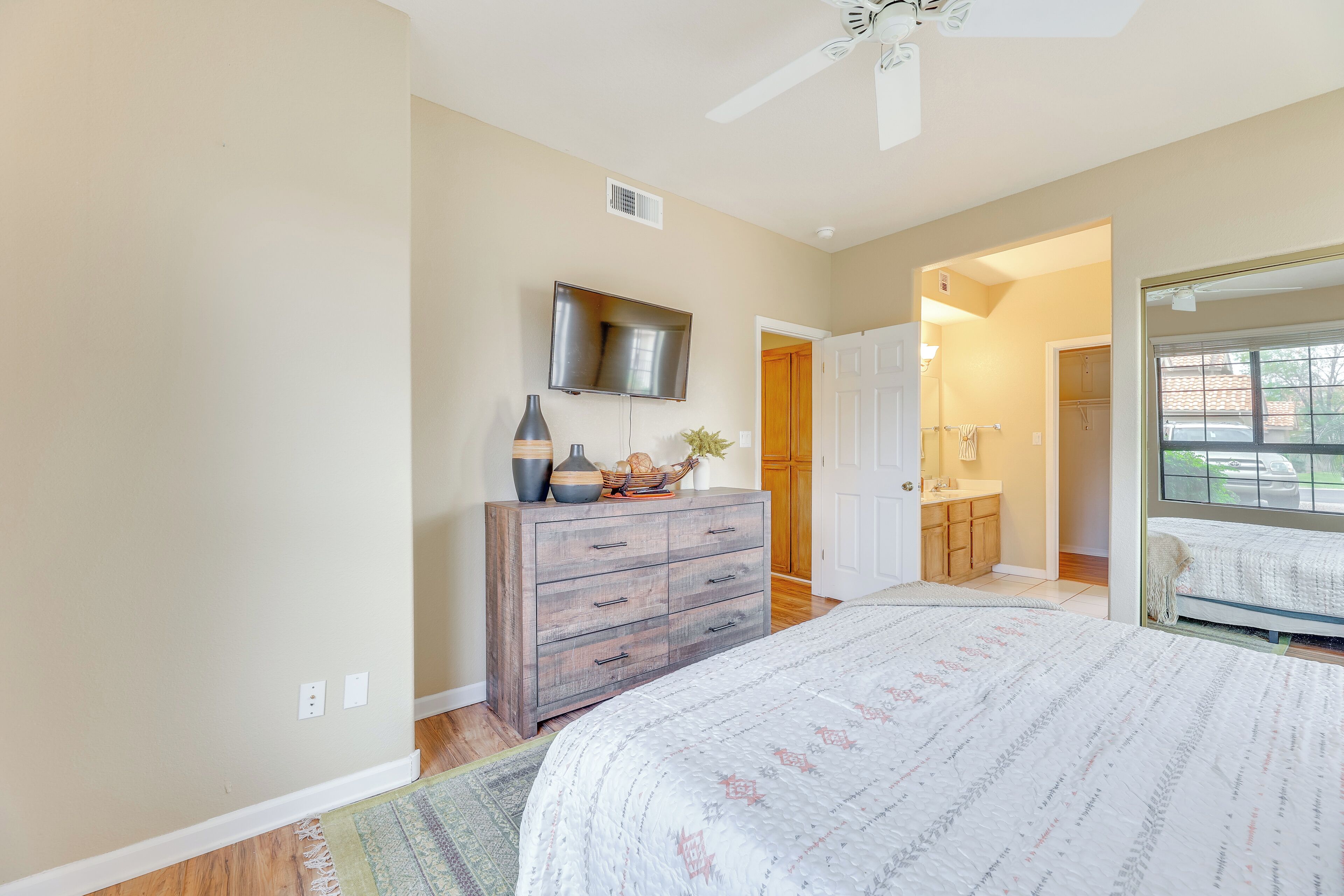 A bedroom with a bed, dresser, TV, and a door leading to a bathroom.
