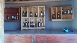 A bar area with wooden shelves displaying bottles, a cash register, and two wooden chairs. - Shanatsi Safari Lodge (Phalaborwa)