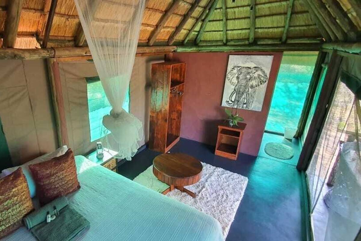 Ein Zelttyp-Zimmer mit einem Bett, einem kleinen Tisch, einem Stuhl und einem hängenden Moskitonetz.