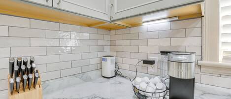 Une cuisine avec des meubles blancs, un plan de travail en marbre, une machine à café et un bloc à couteaux.