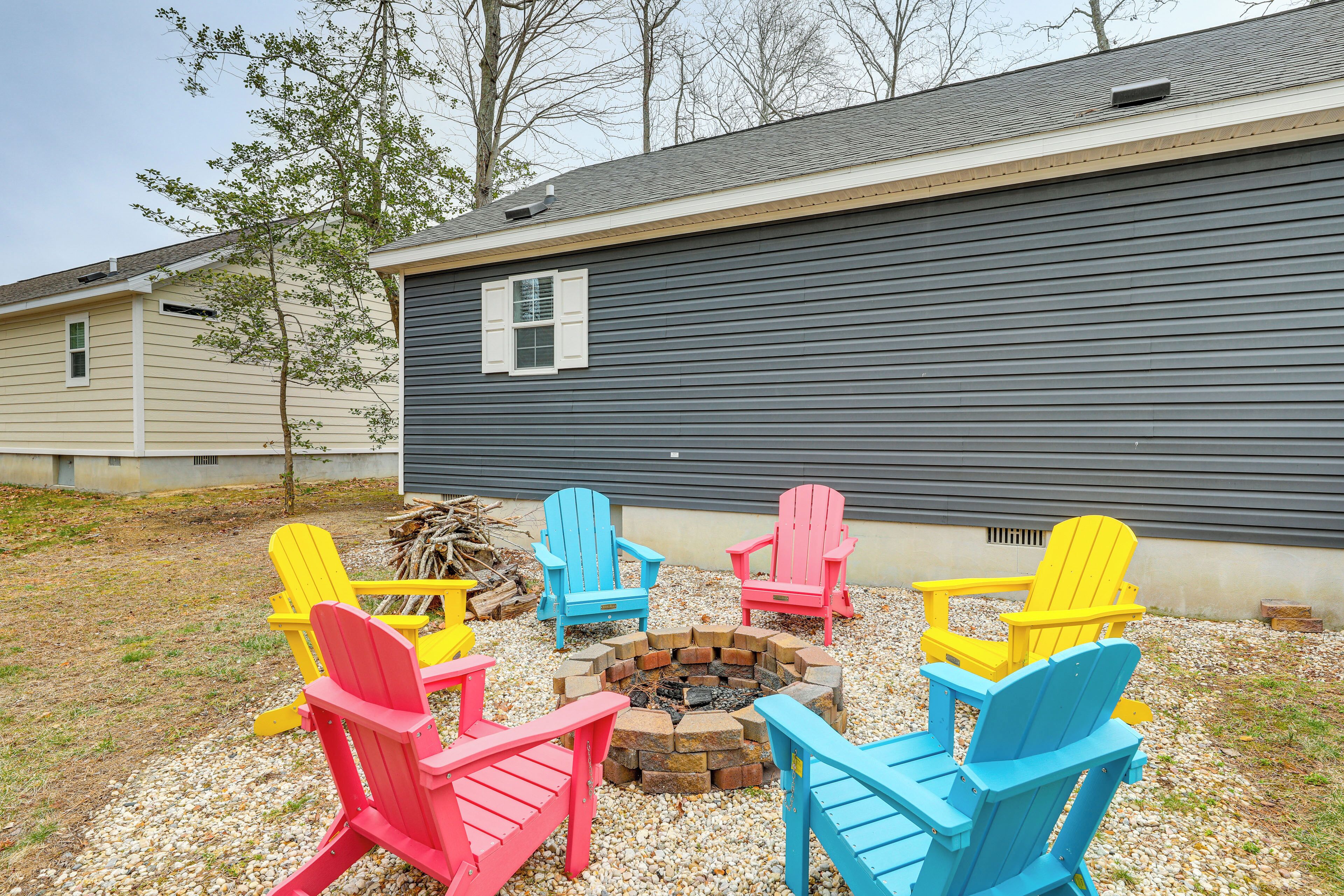 A patio area with colorful Adirondack chairs arranged around a fire pit, set against a residential building with a dark siding exterior.