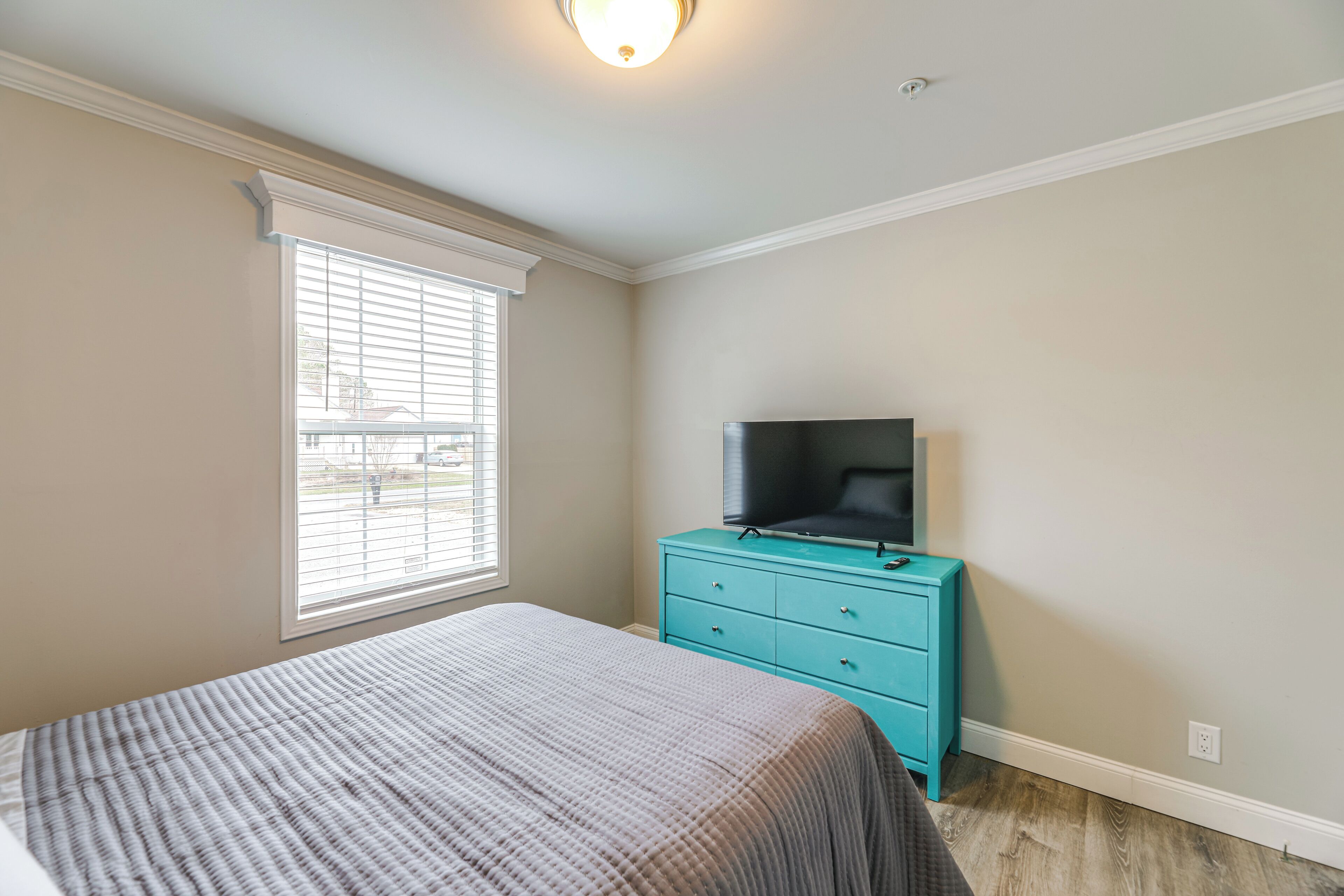 A bedroom with a bed, a television on a dresser, and a window with blinds.