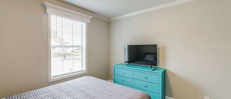 A bedroom with a bed, a television on a dresser, and a window with blinds.