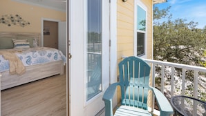 A bedroom with a bed, a chair, and a balcony with a railing.