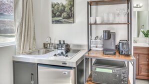 A compact kitchen with a stainless steel refrigerator, a built-in stove, and a coffee maker on a wooden shelf. - 11 Mi to Virginia Beach Boardwalk: Studio Retreat! (Virginia Beach)