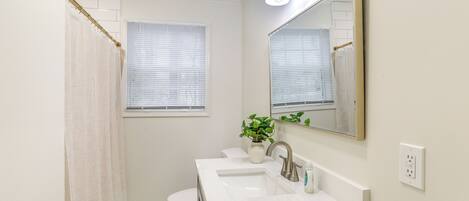 A bathroom with a white sink, a mirror, a toilet, and a shower curtain.