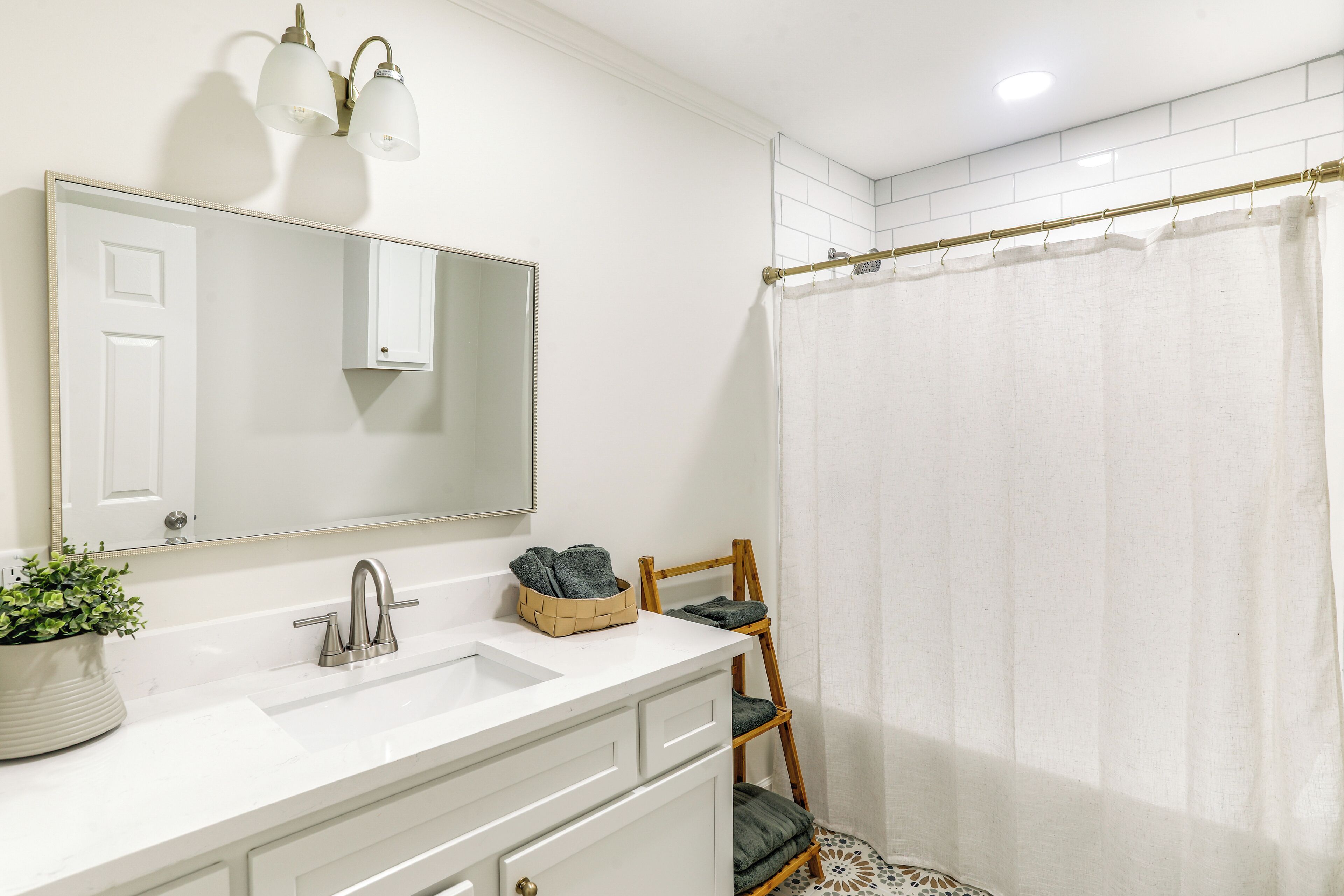 A bathroom with a white vanity, a mirror, a sink, and a shower curtain.