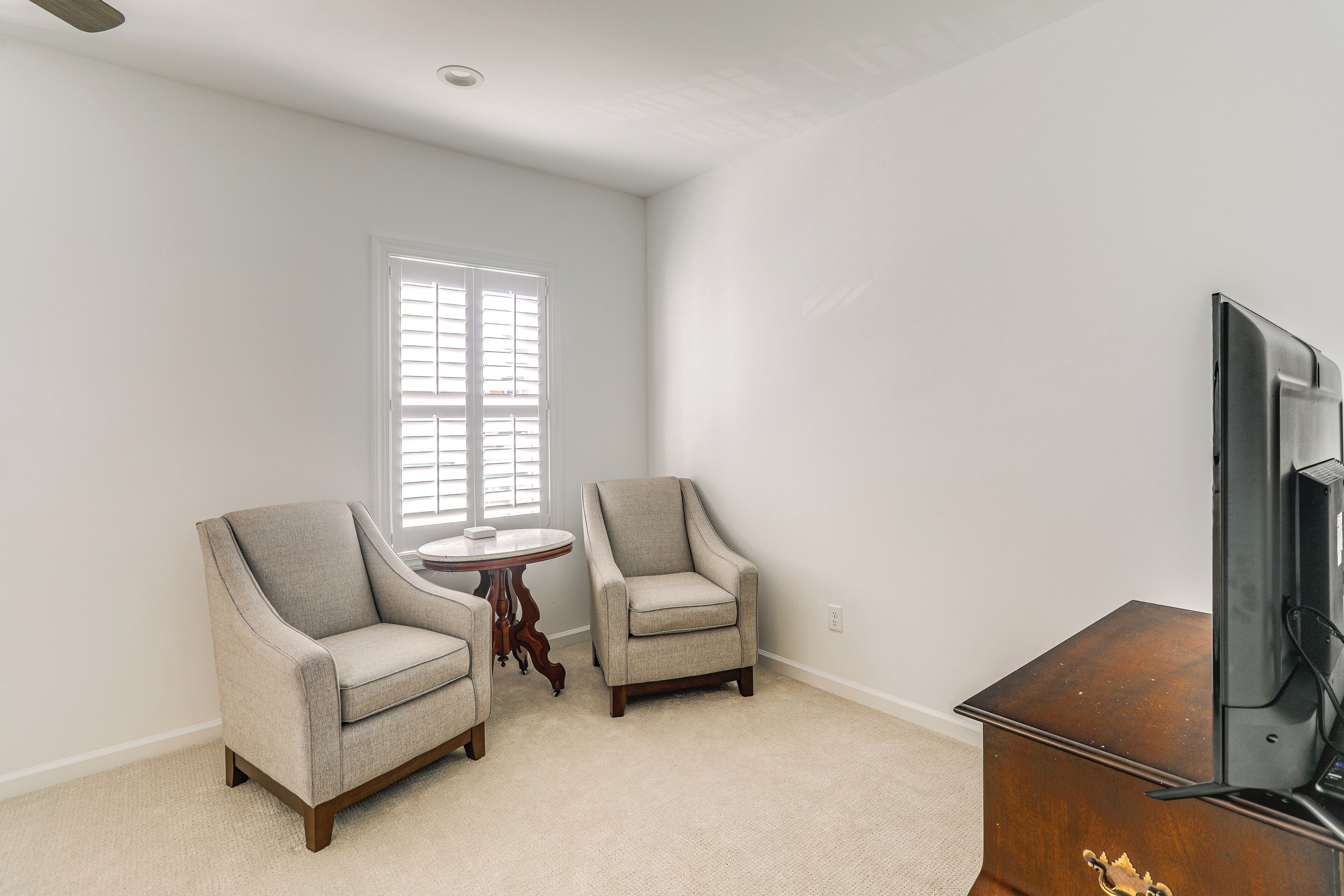 A room with two armchairs, a small round table, a wooden cabinet, and a television.