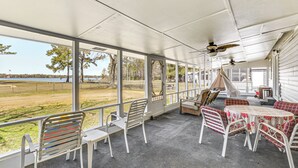 A covered patio with a view of a lake, white metal chairs, a table with a floral tablecloth, and a ceiling fan. - Lake Moultrie Access: Moncks Corner Home w/ Dock (Moncks Corner)