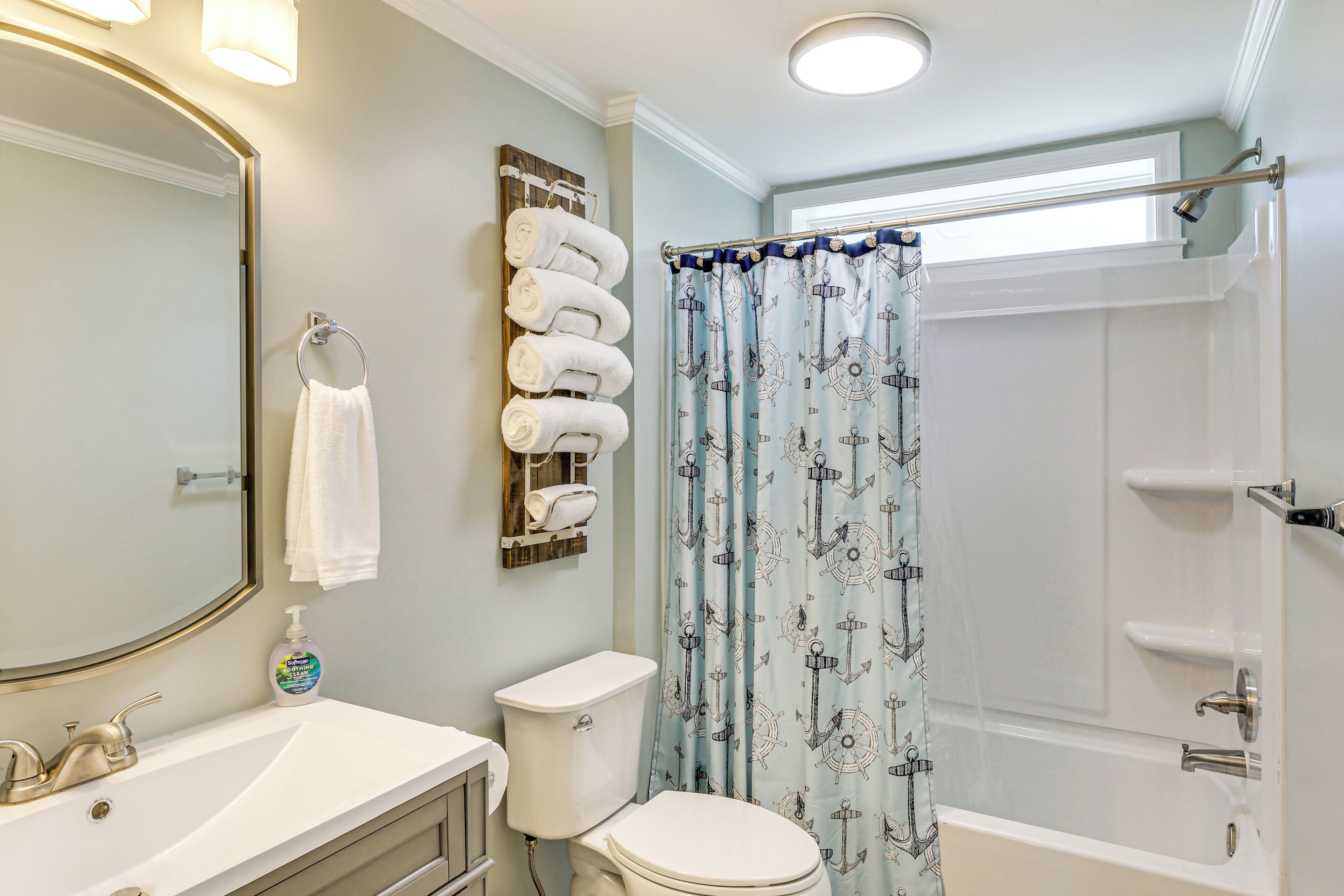 Un baño con lavamanos blanco, inodoro y cortina de ducha con motivos náuticos.