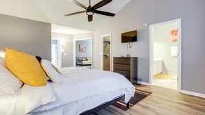 A bedroom with a bed, a ceiling fan, a TV mounted on the wall, and a bathroom visible through an open door. - Close to Shopping: Pet-friendly Lawrenceville Home (Lawrenceville)