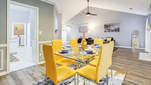 A modern dining area with a glass table and yellow chairs, a ceiling fan, and a cityscape painting on the wall. - Close to Shopping: Pet-friendly Lawrenceville Home (Lawrenceville)