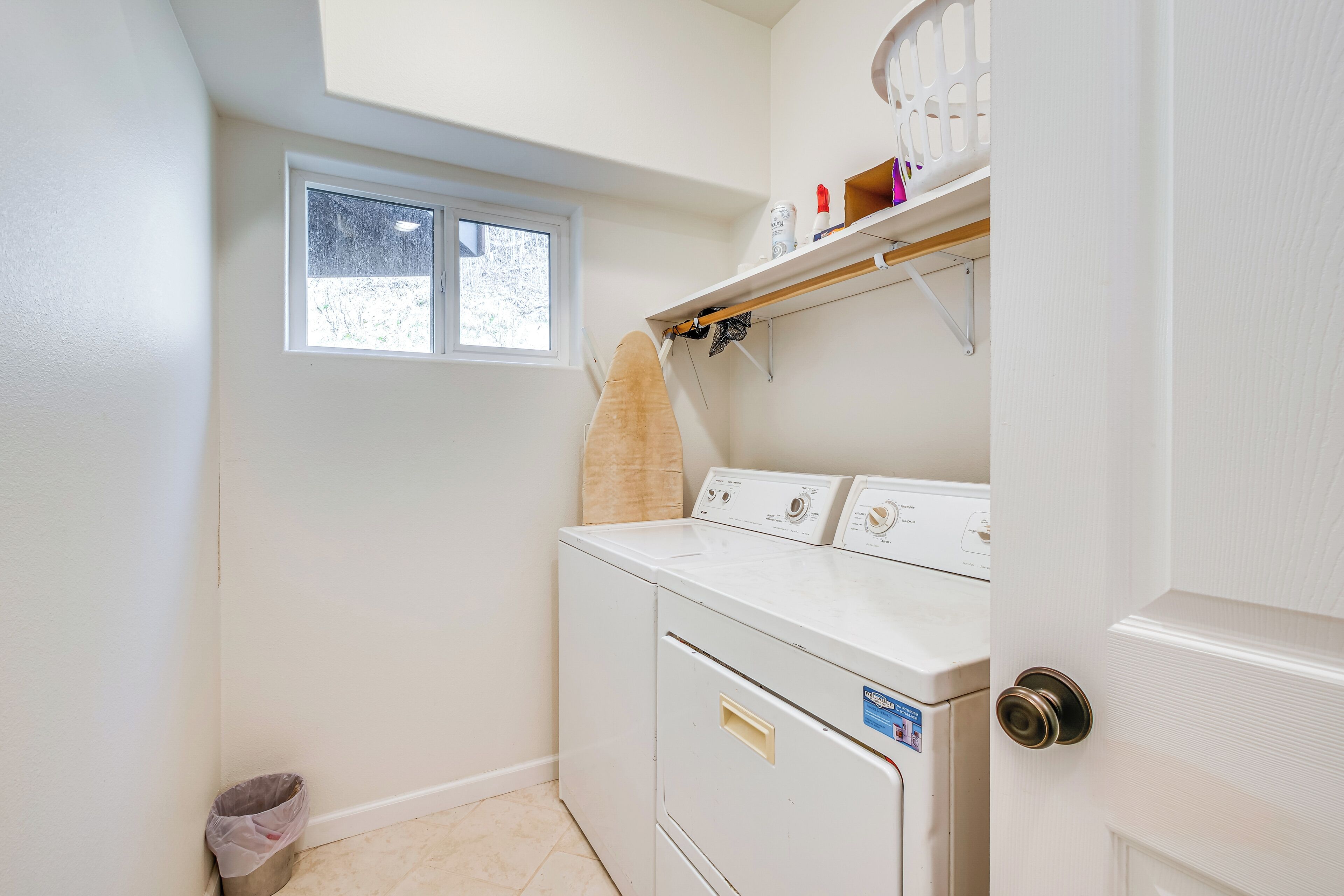 A laundry room with a washer and dryer, a small window, and a shelf with cleaning supplies.