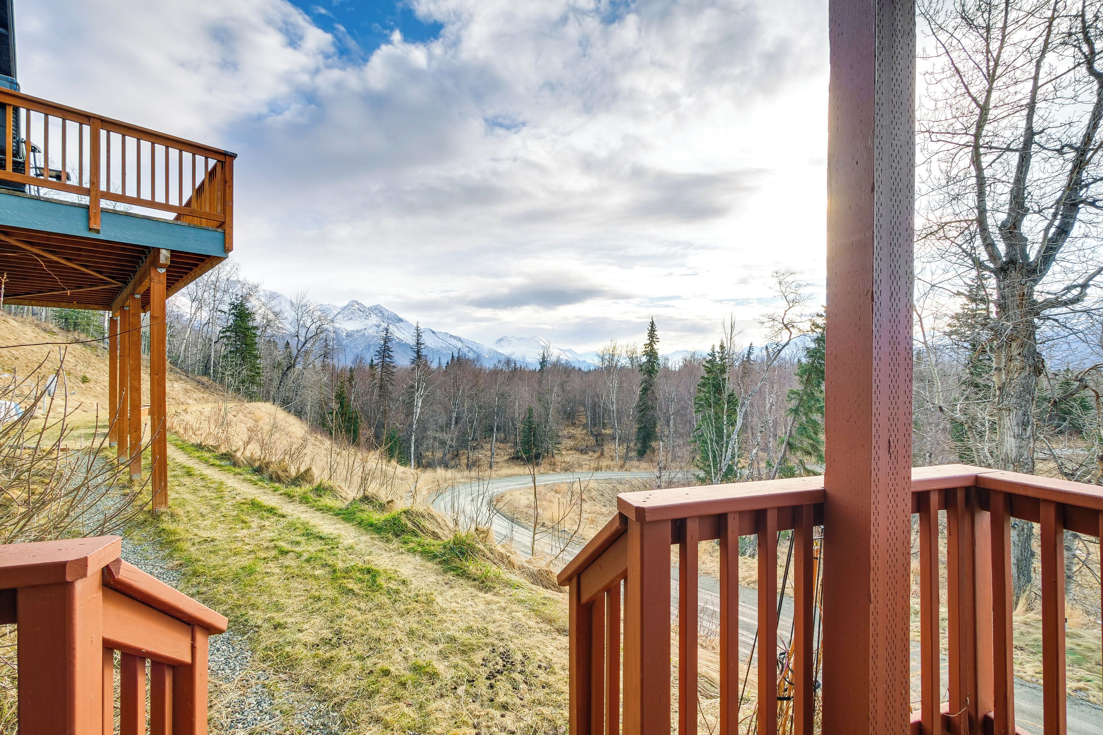 A wooden deck with a view of a winding road and snow-capped mountains in the distance.