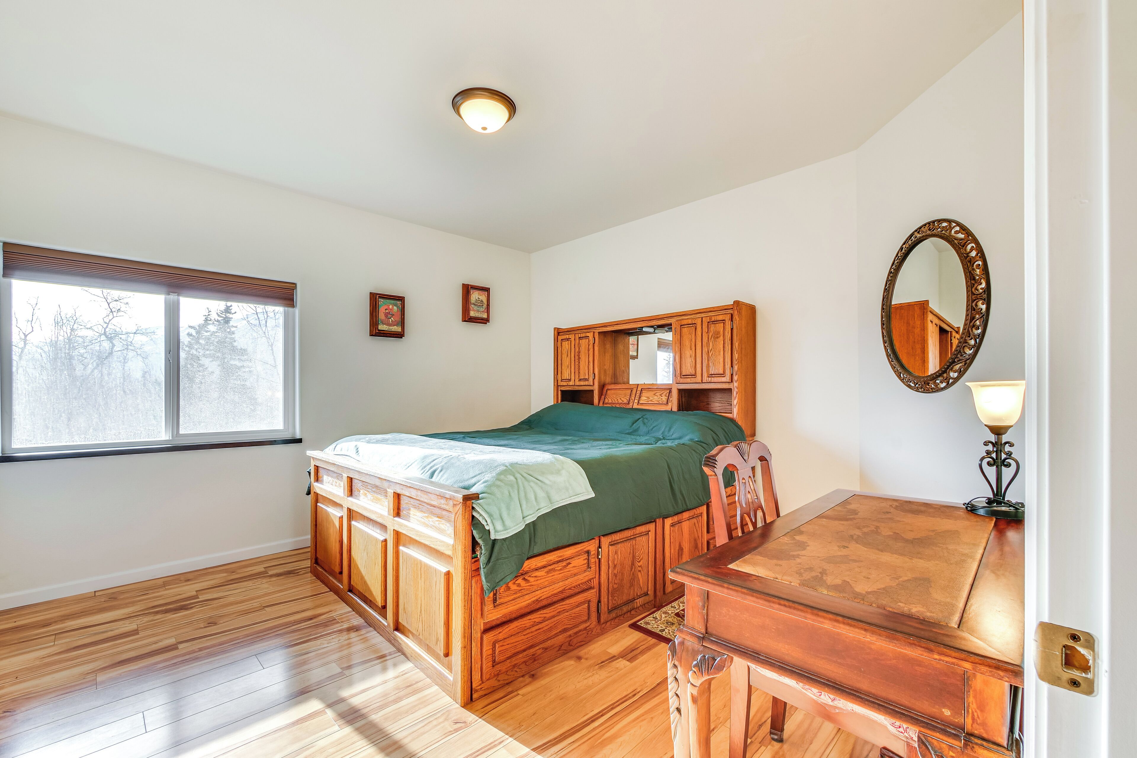 Une chambre à coucher avec un lit en bois, une commode, un miroir et une fenêtre avec des stores.