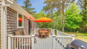 Une terrasse avec une table et des chaises, un barbecue et une rambarde blanche.