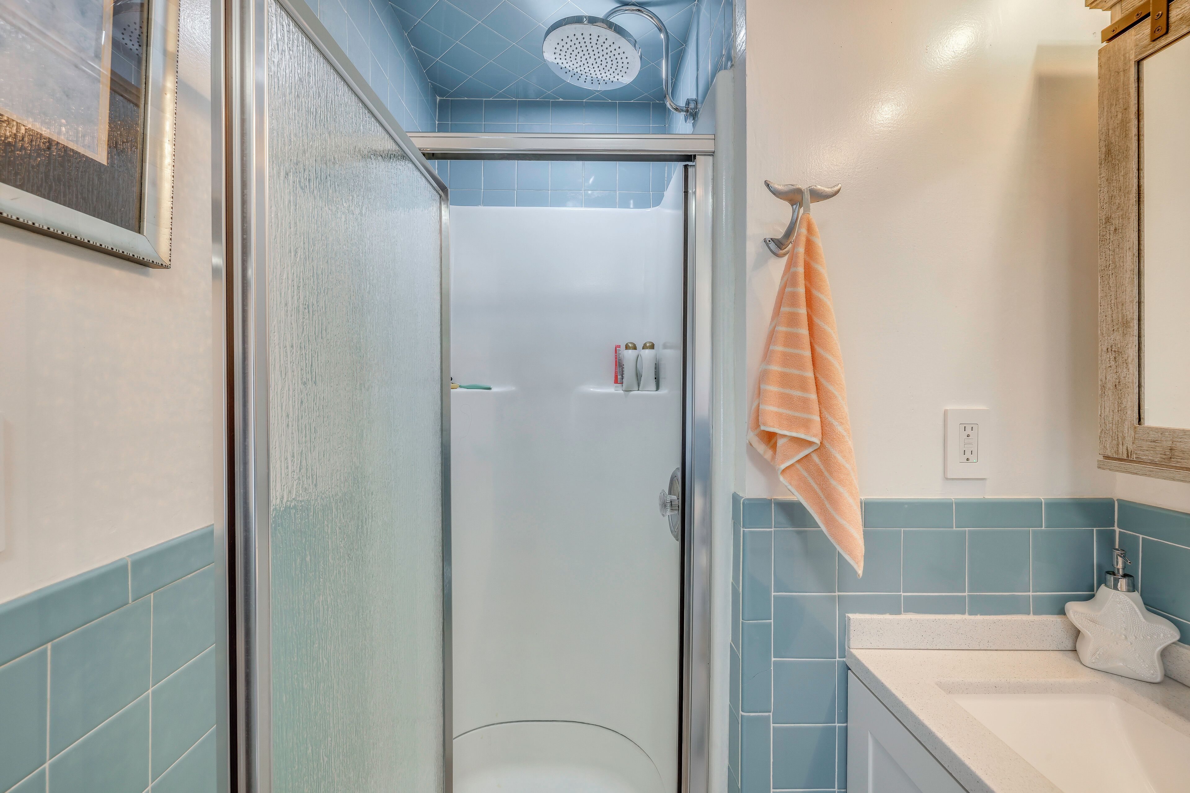 A bathroom with a glass shower enclosure, a white sink, and a towel rack with a striped towel.