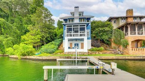 Een steiger die leidt naar een huis met een toren, omgeven door weelderige begroeiing en een rustig wateroppervlak.