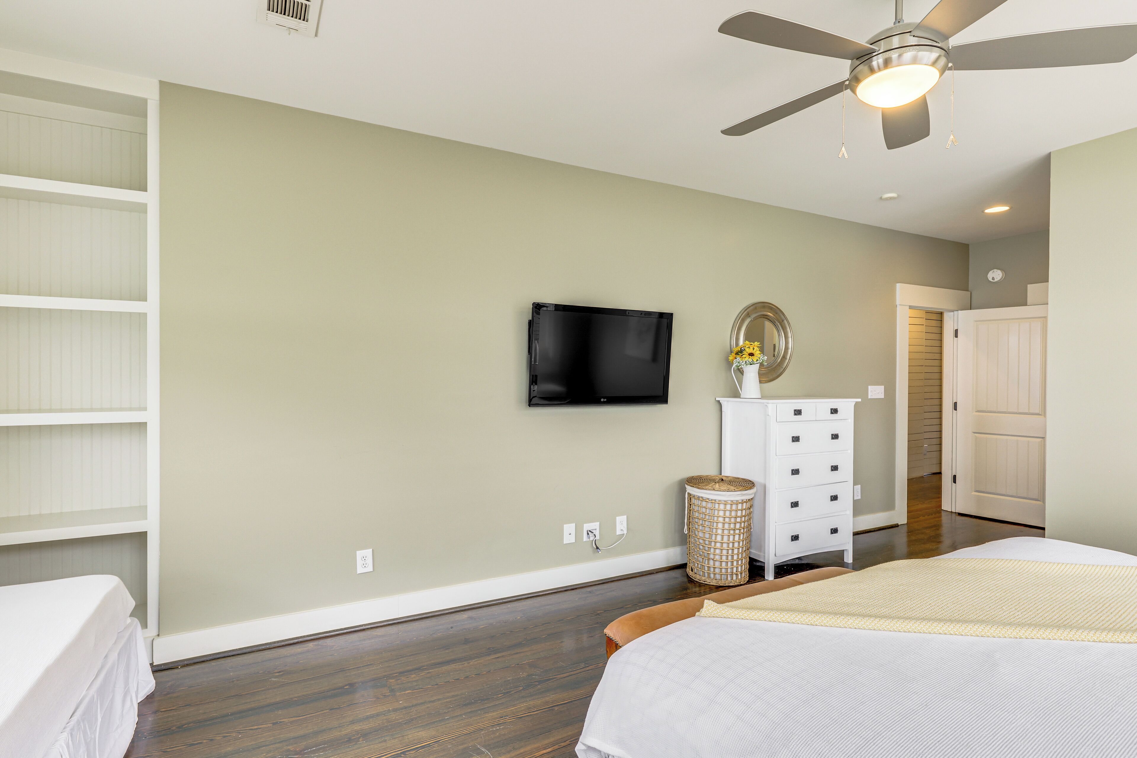 Une chambre à coucher comprenant un lit, une commode, un téléviseur fixé au mur et un ventilateur de plafond.